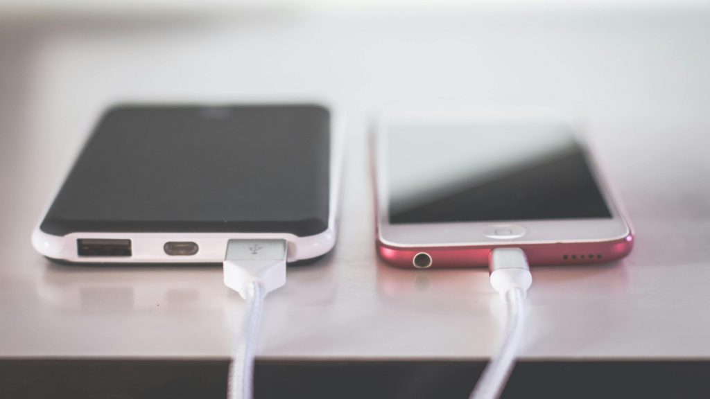 android and iPhone sitting on a table plugged in and charging